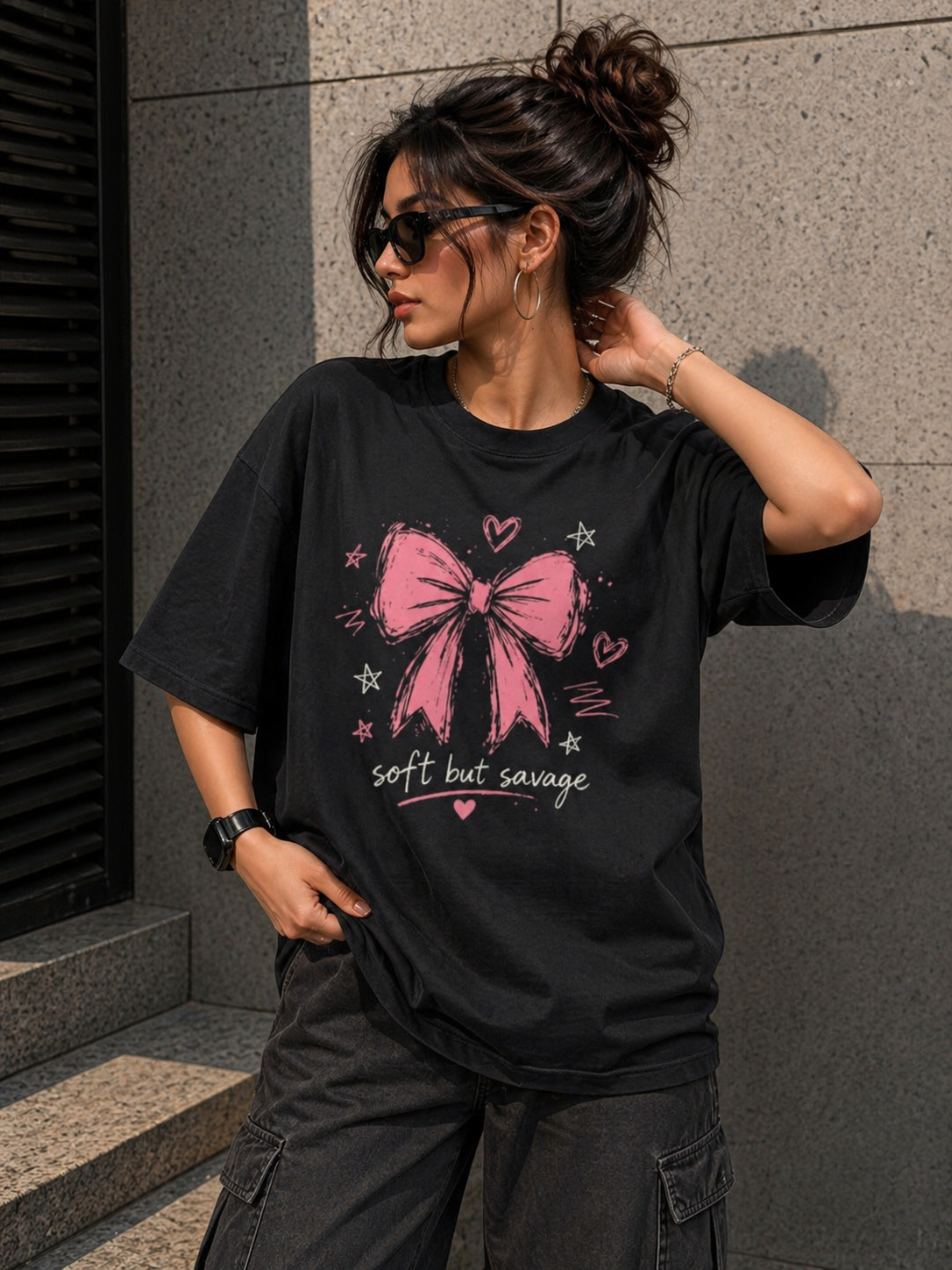 Woman wearing a black oversized graphic t-shirt with a pink bow design, styled for a modern urban look.